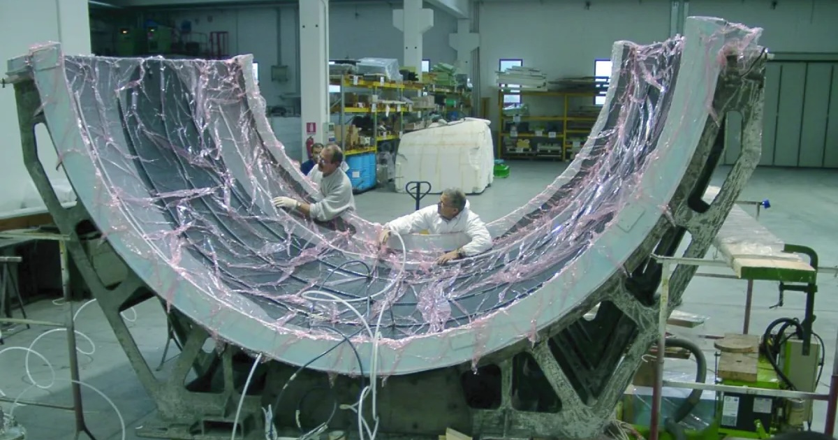 Technicians using vacuum infusion materials on a large curved composite mould